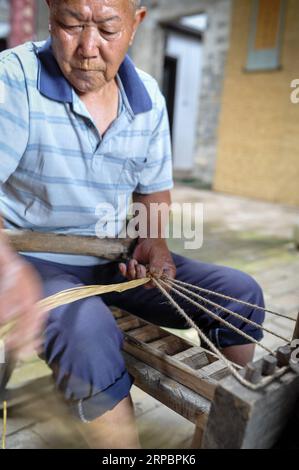 (190614) -- YUDU, 14 giugno 2019 (Xinhua) -- l'artigiano di sandali di paglia Xiao Nandou lavora su sandali di paglia nel villaggio di Hanxin, nella contea di Yudu nella provincia del Jiangxi della Cina orientale, 13 giugno 2019. Xiao Nandou, 75 anni, è uno dei pochi artigiani in grado di tessere sandali di paglia nella contea di Yudu. Suo padre, anche lui un artigiano di sandali di paglia, usava tessere 200 paia di sandali di paglia insieme ad altri abitanti del villaggio in pochi giorni affinché i soldati dell'Armata Rossa partissero per la lunga marcia, una manovra militare condotta dai lavoratori cinesi e dall'Armata Rossa contadina dal 1934 al 1936. (Xinhua/li Renzi) CINA-JIANGXI-LONG MARCH- Foto Stock