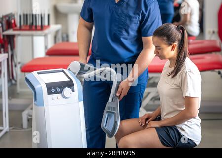 Medico che utilizza la macchina per trattare le articolazioni del ginocchio di un paziente. Foto Stock