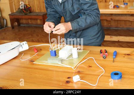 Un elettricista lavora, raccoglie il circuito elettrico di un grande lampione bianco con fili, un relè in una fabbrica industriale. Foto Stock