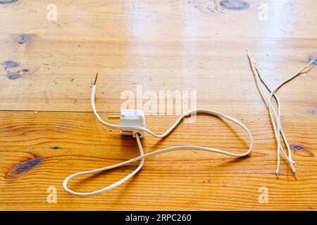 Cavi elettrici pendenti bianchi con una spina elettrica per una presa su un tavolo di legno. Foto Stock