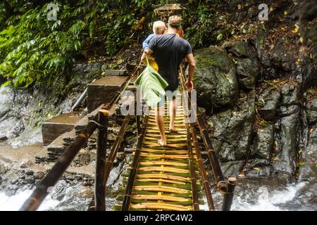 Padre e figlio camminano attraverso il ponte di bambù, Kintamani, Bali, Indonesia Foto Stock