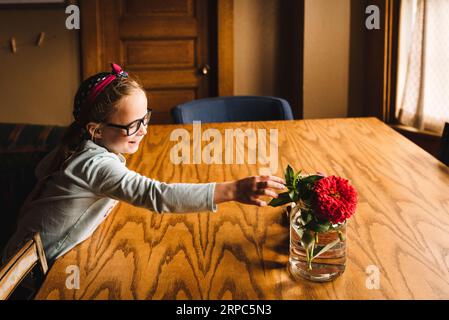 La bambina sorride mentre cerca fiori in vaso sul tavolo Foto Stock