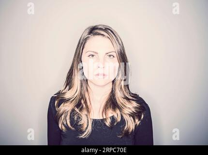 Una giovane donna di fronte a un muro bianco che sembra serio e intenso Foto Stock