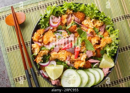 Yam Naem Khao Tod insalata piccante di maiale fermentato con riso croccante, servita con primi piani di verdure sul piatto sul tavolo. Vista dall'alto orizzontale da abov Foto Stock