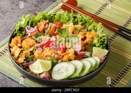 Yam Naem Khao Tod insalata piccante di maiale fermentato con riso croccante, servita con primi piani di verdure sul piatto sul tavolo. Orizzontale Foto Stock