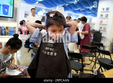 (190629) -- QINGDAO, 29 giugno 2019 -- Un giovane volontario si prepara a lavorare presso la libreria Zhanqiao di Qingdao, nello Shandong della Cina orientale, 29 giugno 2019. Più di 30 bambini sono stati addestrati come volontari nella libreria Zhanqiao. Durante le vacanze estive, saranno impegnati nella guida dei lettori, nella smistamento di libri, nelle attività di welfare pubblico e in altre attività che rientrano nella loro capacità. In cambio, viene loro concessa la priorità nel prendere in prestito libri, con alcuni dati loro come regali. ) CHINA-QINGDAO-LIBRERIA-VOLONTARI (CN) LixZiheng PUBLICATIONxNOTxINxCHN Foto Stock