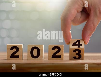 Inizio del nuovo anno 2024. L'uomo d'affari gira a mano cubi di legno da 2023 a 2024 su sfondo lucido. Felice anno nuovo, nuovo business, piano, obiettivi, str Foto Stock