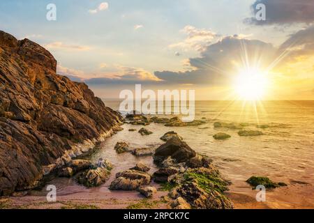 grandi rocce e alghe marine sulla costa rocciosa del mare al tramonto. splendido paesaggio marino alla luce della sera. nuvole sopra l'orizzonte Foto Stock