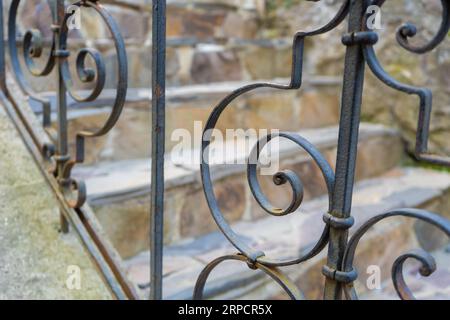 Bella ringhiera decorativa in ferro nero scolpita vicino alle scale di pietra all'esterno nelle giornate di sole da vicino. Concetto di opera d'arte fabbro. Foto di alta qualità Foto Stock