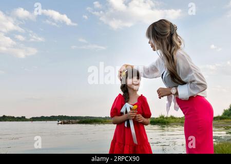 Mamma e figlia stanno camminando vicino al lago o allo stagno. Madre che fissa i capelli della bambina Foto Stock