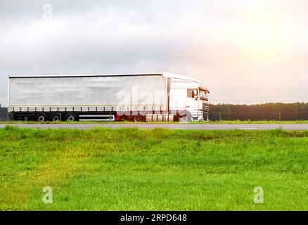 Un veicolo con semirimorchio trasporta il carico in estate su un'autostrada in caso di pioggia, industria Foto Stock