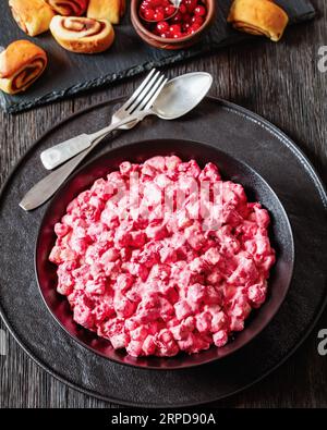 Insalata cremosa di mirtilli rossi con mini marshmallow, mela fresca e noci pecan in ciotola nera su tavola di legno scuro con panini alla cannella, ricetta di Natale, verdura Foto Stock