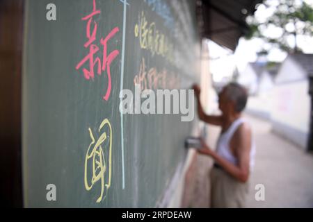 (190801) -- HEXIAN, 1 agosto 2019 -- Ye Lianping scrive abstract di notizie su una lavagna fuori dall'aula della casa per i bambini lasciati nel villaggio di Buchen nella contea di Hexian, nella Cina orientale, provincia di Anhui, 31 luglio 2019. YE Lianping, un insegnante in pensione di 92 anni nel villaggio di Buchen nella contea di Hexian, ha costruito la casa per i bambini lasciati nel 2000 per insegnare loro lezioni di inglese gratis. Poiché la maggior parte dei giovani lavora lontano, anziani e bambini vengono lasciati indietro nel villaggio. Senza figli, Ye vive con sua moglie in un bungalow costruito 30 anni fa, dove offre a quei bambini Foto Stock