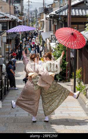 Kyoto, Giappone-14 aprile 2023; primo piano di due ragazze in kimono tradizionale che fanno una posa con gli ombrelli alzati nell'aria nella strada dello storico Hig Foto Stock