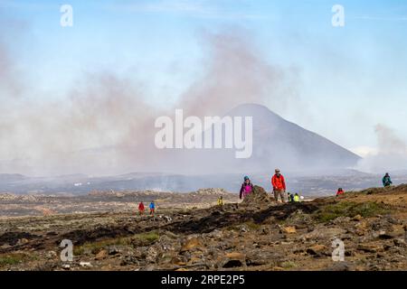 Grindavik, Islanda-28 luglio 2023; persone che camminano vicino alla collina di Litli-Hrútur durante l'eruzione del 2023 vicino alla montagna Fagradalsfjall con il tumulo subglaciale Keilir Foto Stock