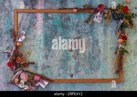 Telaio in legno vuoto con fiori e foglie asciutte su blu Foto Stock