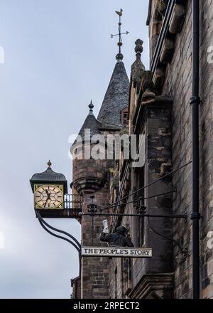 Un orologio classico pende all'angolo di uno splendido edificio con due guglie e una croce in cima, illuminato dalla luce calda del sole che tramonta Foto Stock