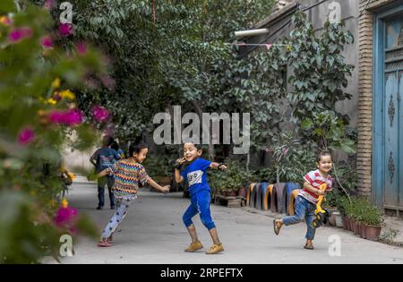 (190828) -- KASHGAR, 28 agosto 2019 -- i bambini si divertono in un vicolo al villaggio di Qianjin a Kashgar, nella regione autonoma di Xinjiang Uygur della Cina nord-occidentale, 18 agosto 2019. Abitazioni circondate da una fioritura profumata in profusione, case ben organizzate e vicoli dall'aspetto pulito, alberi vari che fiancheggiano le strade dove i bambini si divertono, la scena pastorale può essere vista ovunque nel villaggio di Qianjin. La bellezza idilliaca del villaggio di Qianjin deriva dalla sua fioritura economica, in cui Salima Sultan è un pioniere. Salima, un abitante di 60 anni, sviluppò la predilezione dei fiori fin dal filato Foto Stock