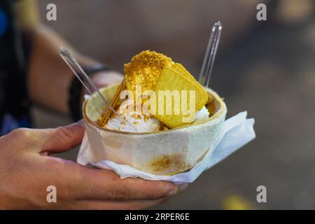 Tenendo a mano il gelato al cocco e al mango in guscio di cocco nel mercato di Street food di Jalan Alor a Kuala Lumpur Foto Stock