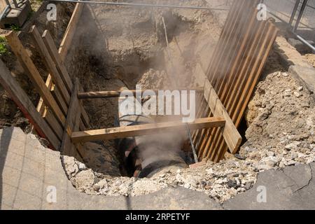 Interrato per il fissaggio di linee di alimentazione dell'acqua calda sotterranea. Dal tubo sotterraneo fuoriesce vapore caldo. acqua bollente in un tubo nel cantiere. Foto Stock