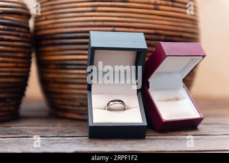 Due anelli placcati oro in eleganti scatole posizionate su un cestino di vimini sul pavimento, ideali per un regalo romantico Foto Stock