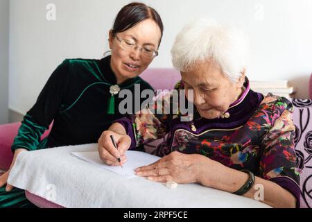 (190913) -- SUIHUA, 13 settembre 2019 -- Jiang Shumei (R) pratica la scrittura sotto la direzione di sua figlia a casa nel distretto di Beilin della città di Suihua, nella provincia di Heilongjiang nella Cina nordorientale, 12 settembre 2019. Nato nel 1937, Jiang era analfabeta prima dei 60 anni. Per alleviare la sofferenza di Jiang dopo la morte del marito nel 1996 in un incidente d'auto, sua figlia Zhang Lailing ha insegnato alla donna anziana a leggere e scrivere da allora. Con l'incoraggiamento di sua figlia, Jiang ha cercato di scrivere un libro. Nel 2013 fu pubblicato il primo libro di Jiang. Finora, lo scrittore di 82 anni ha pubblicato cinque libri e ha vinto Foto Stock