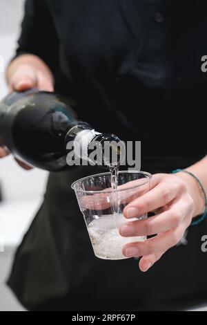 Cameriere inriconoscibile che serve champagne in una tazza di plastica Foto Stock