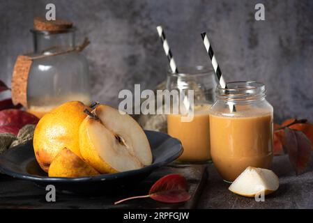 Spremuta fresca, gustosa, biologica, sana succo di pera, in vasetti di vetro con tubi bianchi e neri, e un pezzo di pera tagliata a fette , su uno schienale grigio Foto Stock