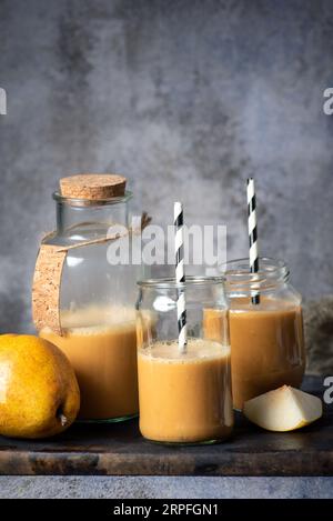 Spremuta fresca, gustosa, biologica, sana succo di pera, in vasetti di vetro con tubi bianchi e neri, e un pezzo di pera tagliata a fette , su uno schienale grigio Foto Stock