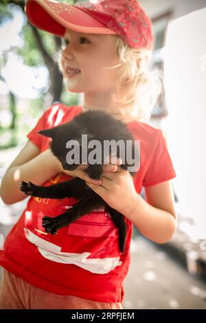 Una bambina tiene un gattino randagio nero. Un bambino ha adottato un animale da un rifugio. Foto Stock