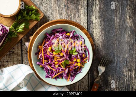 Concetto di cibo vegano, cibo sano. Insalata di cavolo viola fatta in casa con mais, carote e yogurt greco su un tavolo rustico. Vista dall'alto. Copia spazio. Foto Stock