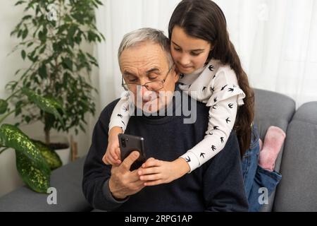 Ragazza adolescente che scatta foto con il telefono cellulare di se stessa e suo nonno. Foto Stock