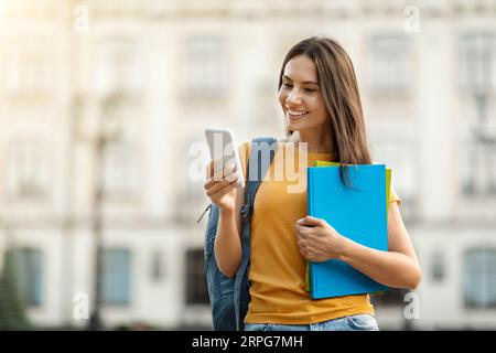 Studentessa sorridente con smartphone e cartelle di lavoro che si rilassano all'aperto Foto Stock