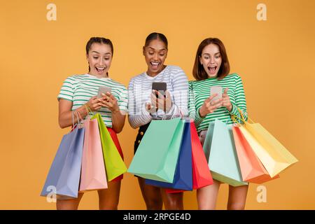 Stupite tre giovani donne multietniche che fanno acquisti online, utilizzando smartphone Foto Stock