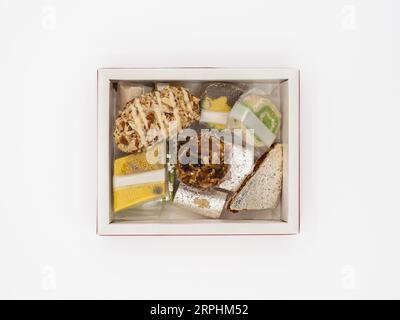 Vista dall'alto di una scatola piena di deliziosi dolci indiani ghee assortiti, isolati su uno sfondo bianco. Foto Stock