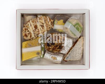 Vista dall'alto di una scatola piena di deliziosi dolci indiani ghee assortiti, isolati su uno sfondo bianco. Foto Stock