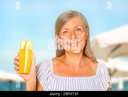 Protezione solare. Bella donna matura con una bottiglia di crema solare sulla spiaggia Foto Stock