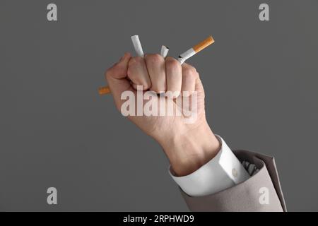 Smettere di fumare. Uomo che frantumava sigarette su sfondo grigio, primo piano Foto Stock