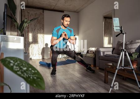 Un uomo latino che fa un video fitness per i social media. Creatore di contenuti o influencer maschile per la formazione online sul fitness. Foto Stock