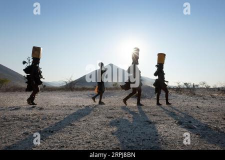 Le donne Himba camminano tutte in una sola fila mentre tornano dalla raccolta dell'acqua. L'acqua è spaventosa nella Namibia settentrionale, quindi tutte le razioni devono essere raccolte su Foto Stock