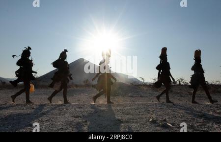 Le donne Himba camminano tutte in una sola fila mentre tornano dalla raccolta dell'acqua. L'acqua è spaventosa nella Namibia settentrionale, quindi tutte le razioni devono essere raccolte su Foto Stock