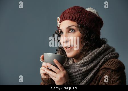 Abbracciata dall'inverno, una donna in abiti di lana sorseggia una bevanda confortante come latte, caffè latte o cioccolato. Si è stabilita in un rifugio di montagna o in un bar, lei g Foto Stock