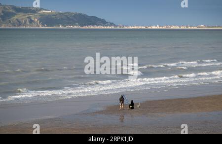 Gente che pesca sulla spiaggia nel Galles del Nord, con Landudno e il Great orme nel backgroup. Galles, Regno Unito. Foto Stock