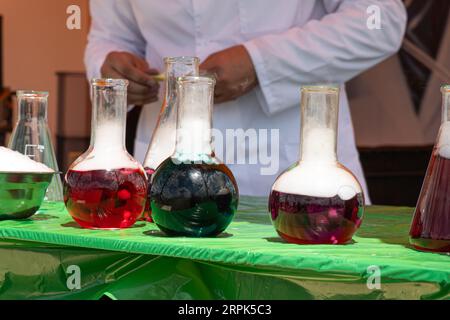Vetreria da laboratorio e provette per analisi con liquidi colorati su un tavolo in vetro all'aperto. Reazione chimica Foto Stock