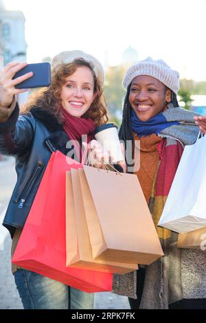 Due amici femminili multirazziali che prendono un selfie con lo smartphone mentre acquistano nel centro della città in inverno. Foto Stock