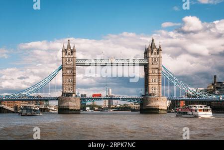 Londra, Inghilterra - 29 luglio 2023: Un iconico autobus rosso di Londra passa sopra il Tower Bridge mentre le navi da crociera passano lungo il Tamigi a Londra, Englan Foto Stock