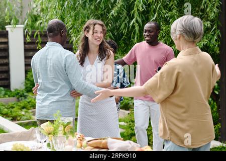 Felice giovane uomo e donna che salutano i genitori interculturali con abbracci e salutano loro mentre visitano la coppia matura nel fine settimana Foto Stock