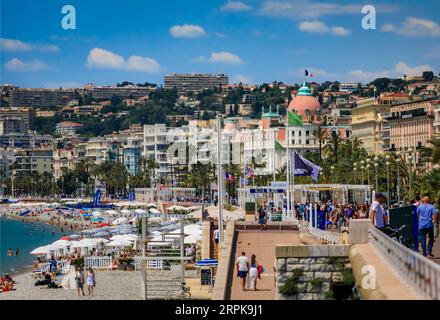 Nizza, Francia - 28 maggio 2023: Gente sulla famosa Promenade des Anglais con costa del Mar Mediterraneo e hotel Negresco sullo sfondo, Costa Azzurra Foto Stock