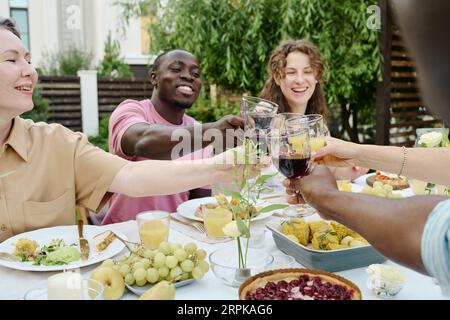 Felice giovane coppia e donna matura che si accarezzano di occhiali da vista di un uomo interculturale e di sua moglie durante un brindisi celebrativo a cena Foto Stock
