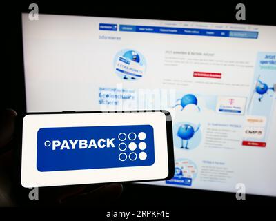 Persona che possiede uno smartphone con il logo della società tedesca di gestione della fidelizzazione Payback GmbH sullo schermo davanti al sito Web. Concentrarsi sul display del telefono. Foto Stock